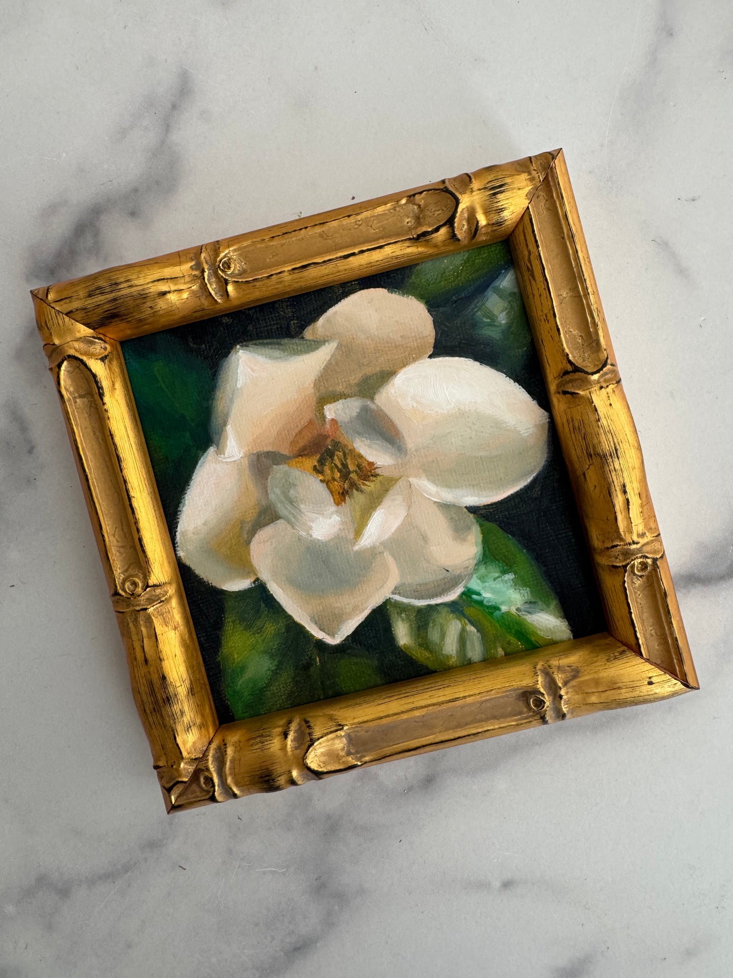 Magnolia IV in its gold bamboo frame on a marble table, angled view